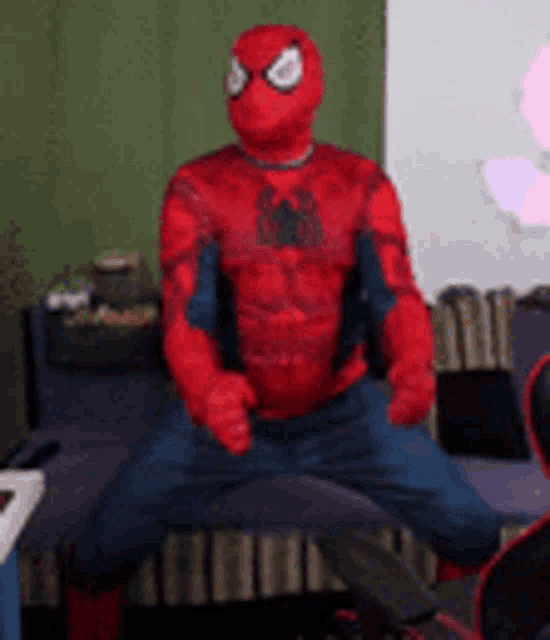 a man dressed in a spiderman costume is sitting on a chair .