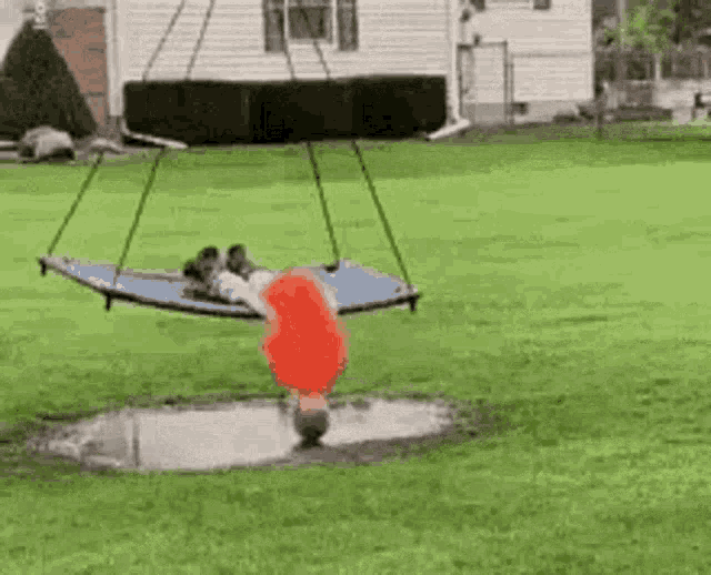 a person is hanging upside down on a swing in a yard .