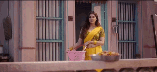 a woman in a yellow sari is standing in front of a building holding a basket .