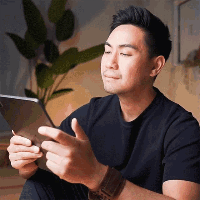 a man in a black shirt is sitting on the floor using a tablet