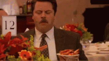 a man in a suit and tie is eating shrimp at a table with flowers .