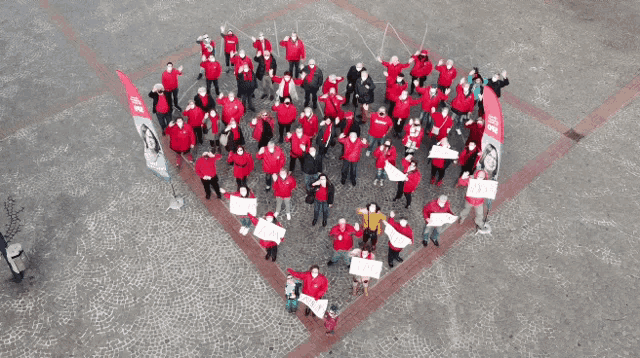 a large group of people are standing in a heart shape holding signs