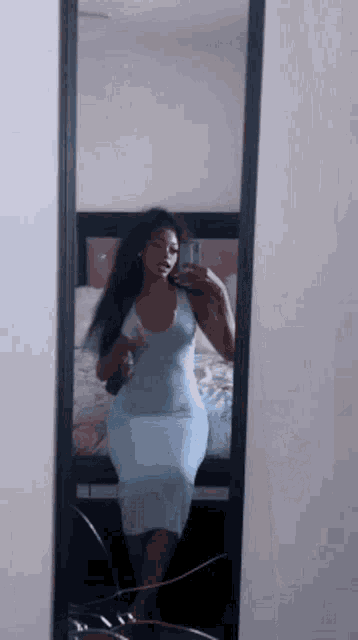 a woman in a blue dress is taking a picture of herself in a mirror .