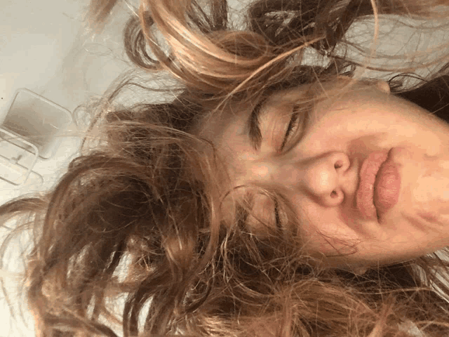 a close up of a woman 's face with her eyes closed and hair blowing in the wind