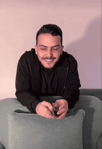 a man with a mustache is sitting on a couch holding a glass