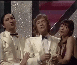 a man in a tuxedo is holding a glass of champagne while standing next to two women .