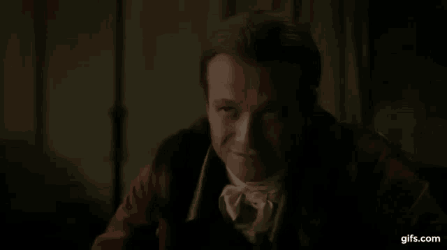 a man in a red coat and tie is talking in a dark room .