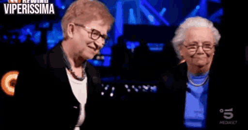 two older women are standing next to each other on a stage and one of them is saying u signur