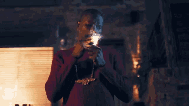 a man wearing a red sweater is lighting a cigarette with a lighter