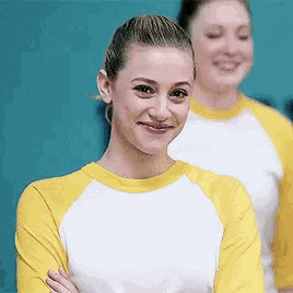 a woman in a yellow and white shirt is smiling with her arms crossed in front of a blue wall .