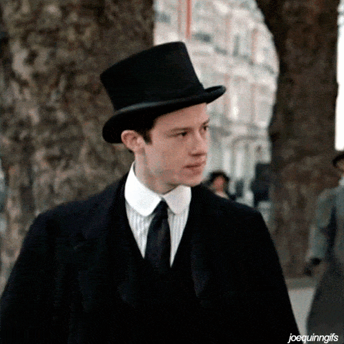 a man wearing a top hat and a suit stands in front of trees