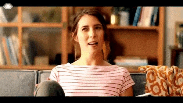 a woman in a pink striped shirt is sitting on a couch with her legs crossed