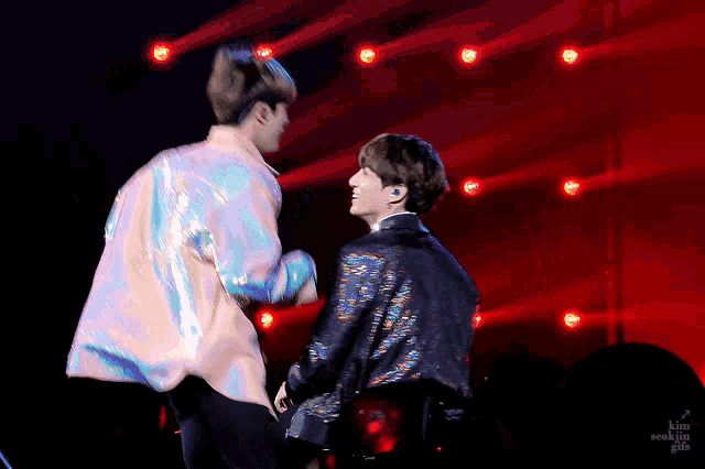a man in a sequined jacket stands next to another man in a white shirt