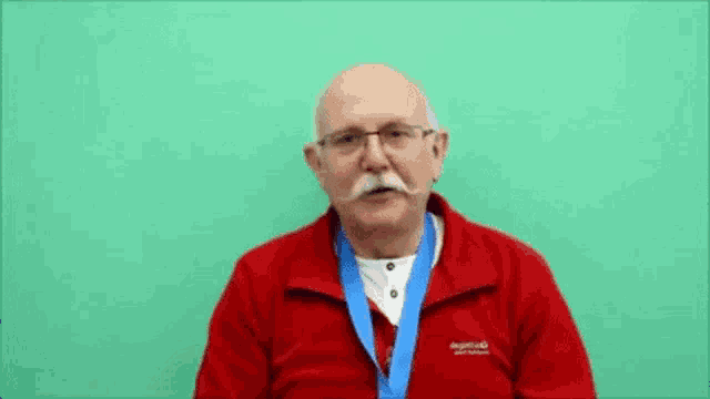 a man wearing a red jacket and a blue medal that says broad beans
