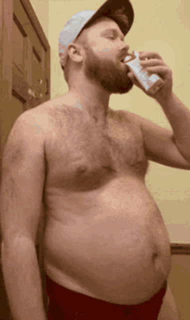 a shirtless man with a beard is drinking from a carton of milk
