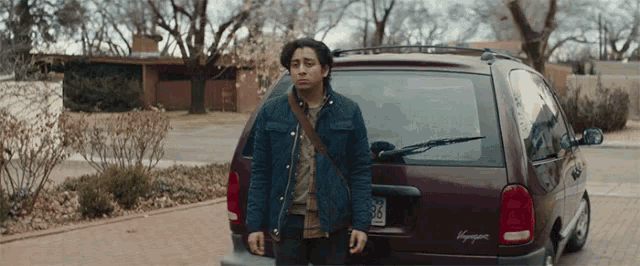 a young man stands in front of a voyager minivan