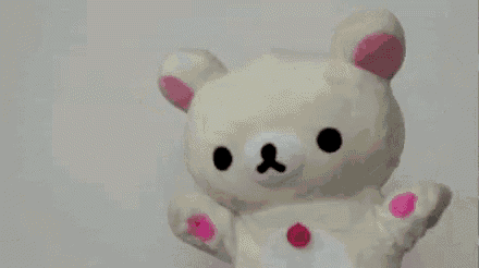 a white teddy bear with pink paint on its face is sitting on a table with a pink piece of paper .
