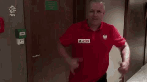 a man is standing in a hallway wearing a red shirt and dancing .