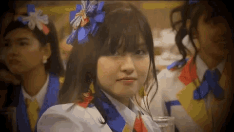 a girl with a blue flower in her hair looks at the camera with other girls behind her