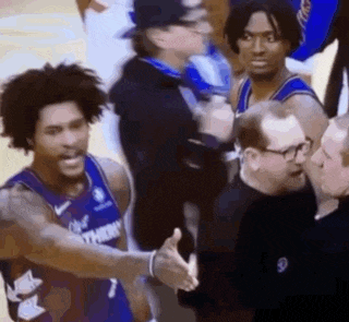 a basketball player is shaking hands with a referee while standing next to a group of men .