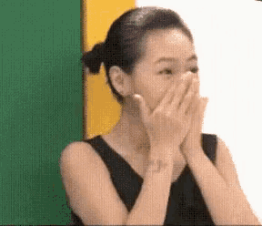 a woman is covering her face with her hands while standing in front of a green and yellow wall .