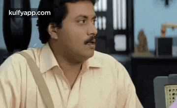 a man with a mustache is sitting at a desk in front of a laptop computer and making a funny face .