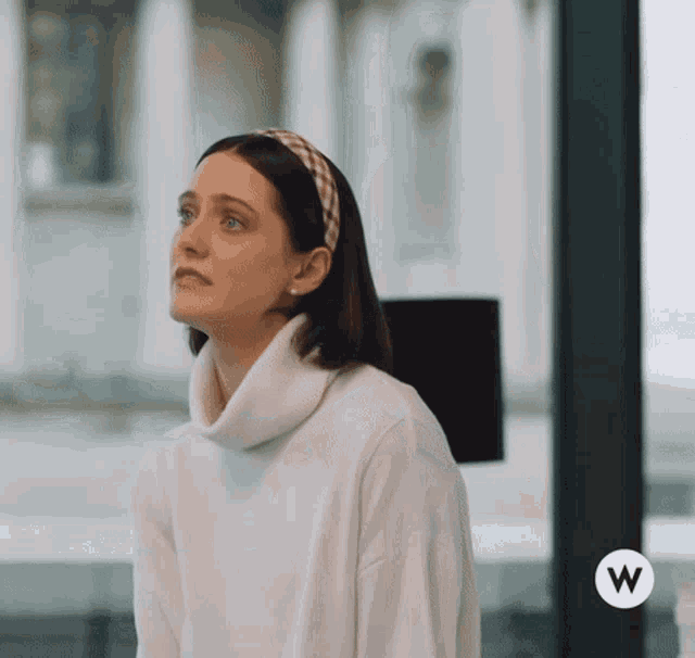 a woman wearing a headband and a white sweater with the letter w on the bottom right
