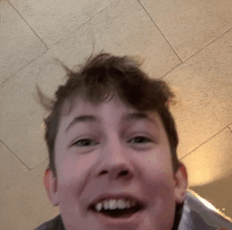a close up of a young man 's face with his mouth open and his hair flying in the air .