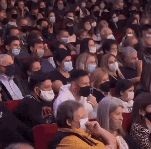a crowd of people wearing face masks are sitting in a theatre .