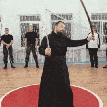 a man in a black robe holds a sword in a gym