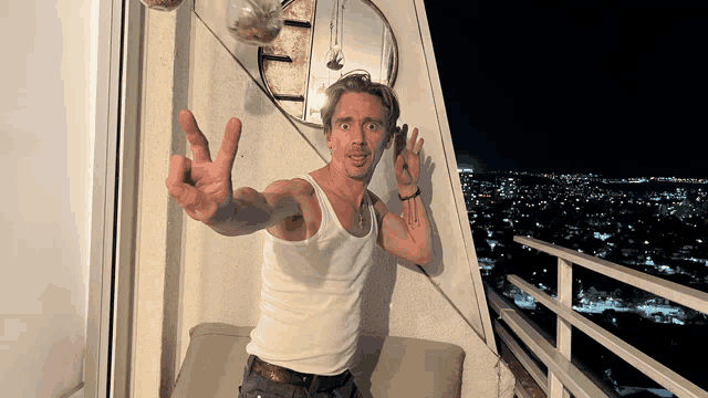 a man in a white tank top gives the peace sign