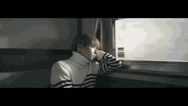 a young man in a striped sweater is looking out a window