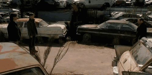 two men are standing in a lot of old cars