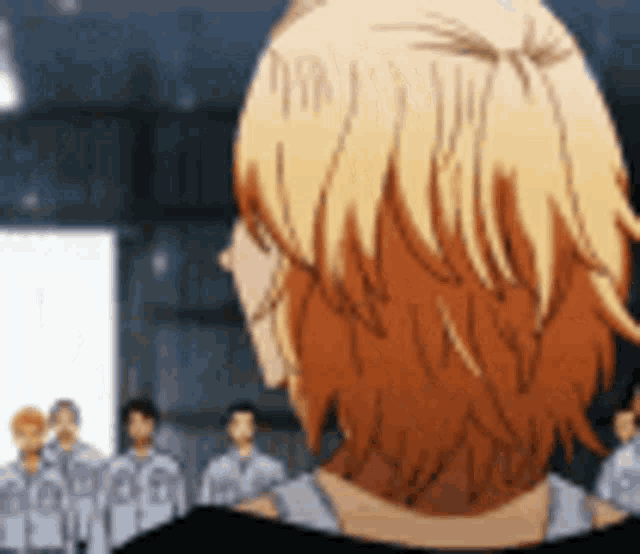a man with blonde hair is looking at a group of people in a room .