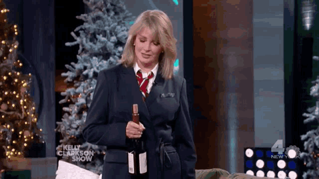 a woman in a suit and tie is holding a bottle of wine on the kelly clarkson show