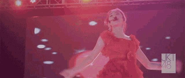 a woman in a red dress is dancing on a stage in front of a screen that says uk 48