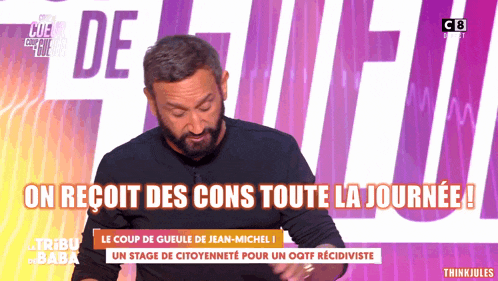 a man with a beard stands in front of a sign that says on reoit des cons toute la journee !