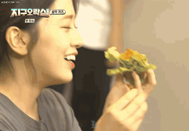 a woman is eating a sandwich with the words honeycam.org on the bottom
