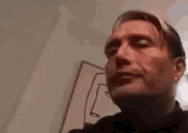 a close up of a man 's face with a drawing of a face on the wall behind him .