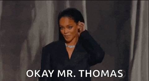 a woman in a suit and a necklace is standing on a stage and saying okay mr. thomas .