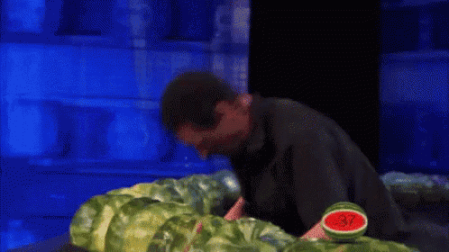 a man in a black shirt is cutting watermelons in half