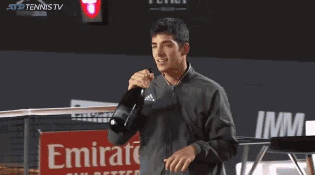 a man is holding a bottle of champagne in front of an emirates sign