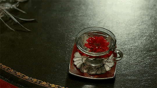 a cup of tea with a red flower in it on a saucer