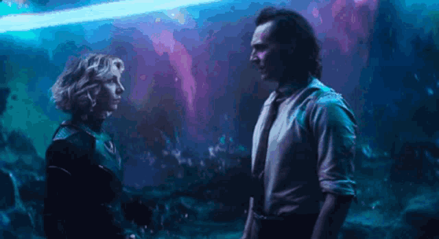 a man and a woman are standing next to each other in a dark room and looking at each other .