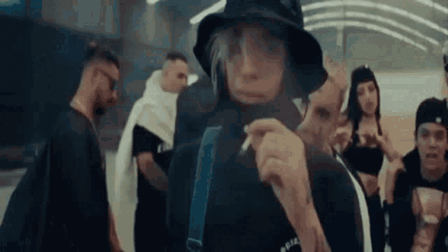 a man in a hat is smoking a cigarette in front of a group of people .