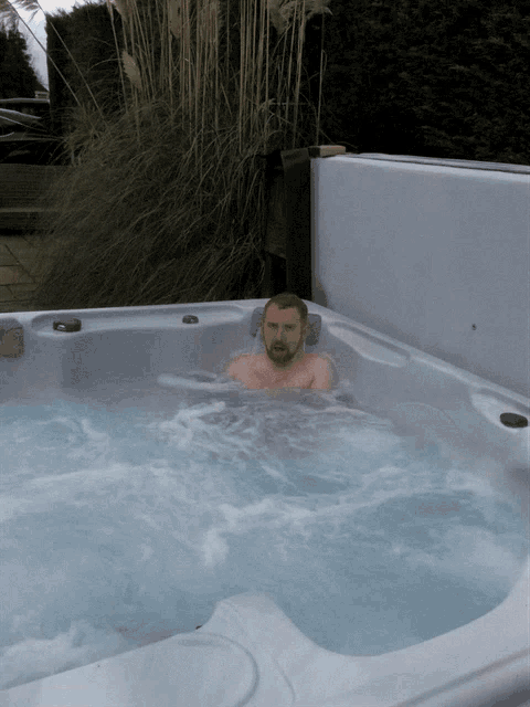 a man is sitting in a hot tub with a plant in the background