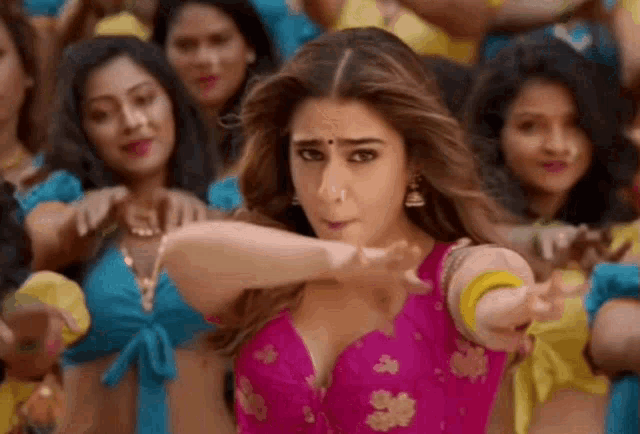 a woman in a pink top is dancing in front of a crowd of women in blue tops .