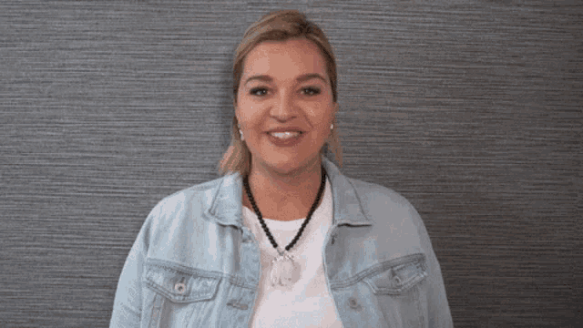 a woman wearing a white shirt and a denim jacket smiles