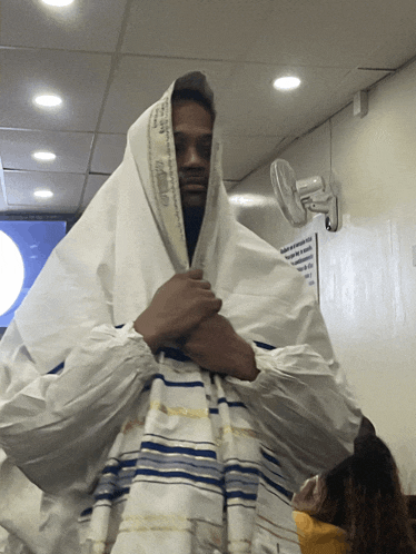 a man is wrapped in a white blanket with a sign on the wall behind him that says ' no smoking ' on it