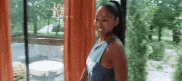 a woman in a tank top is standing in front of a window .